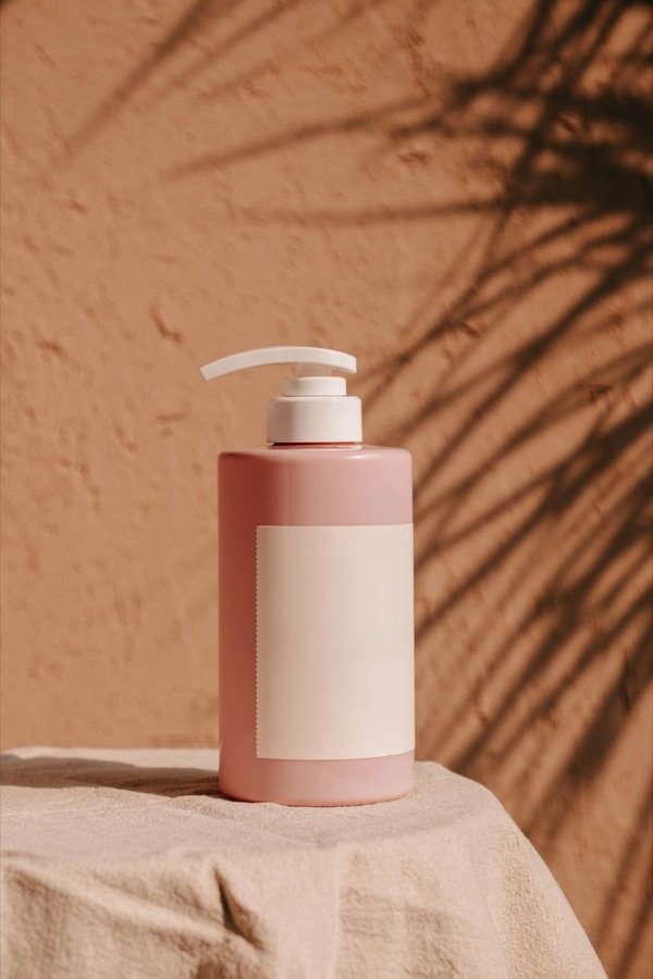 A pink pump bottle photographed against a terracotta wall