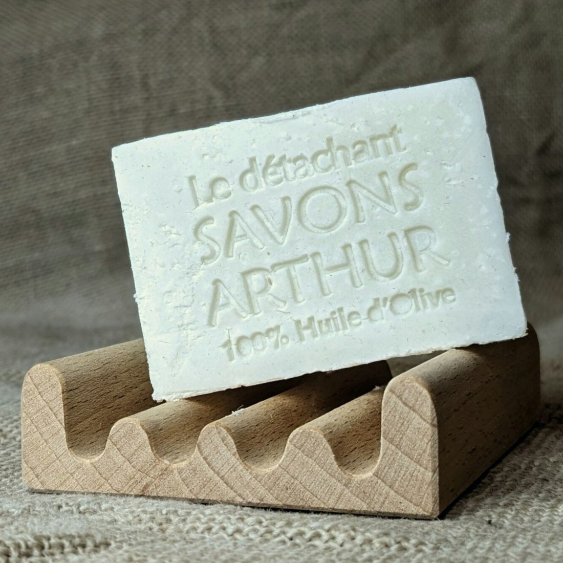 A bar of olive oil soap with its name stamped into it, in a wooden dish